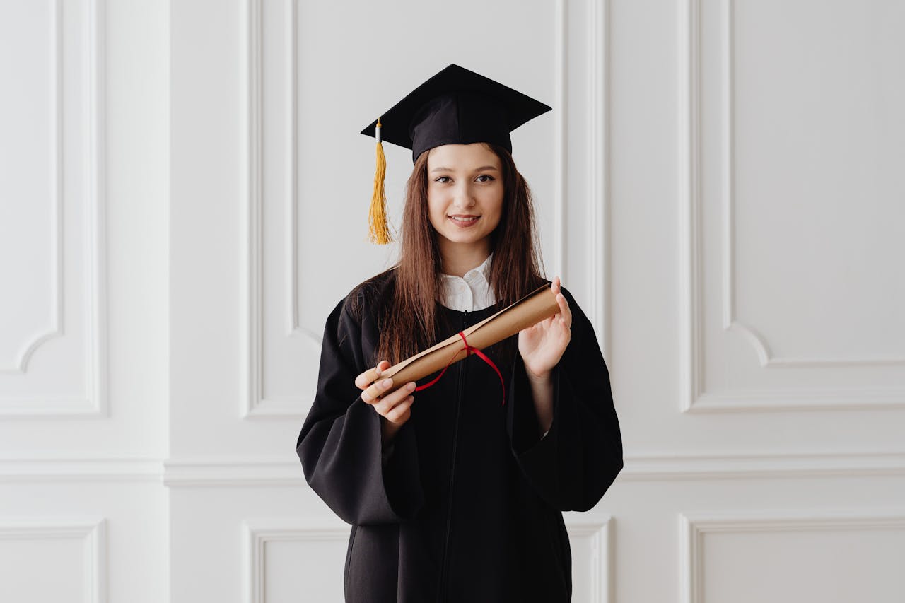 Portrait of a young woman in graduation attire posing with a diploma indoors.
